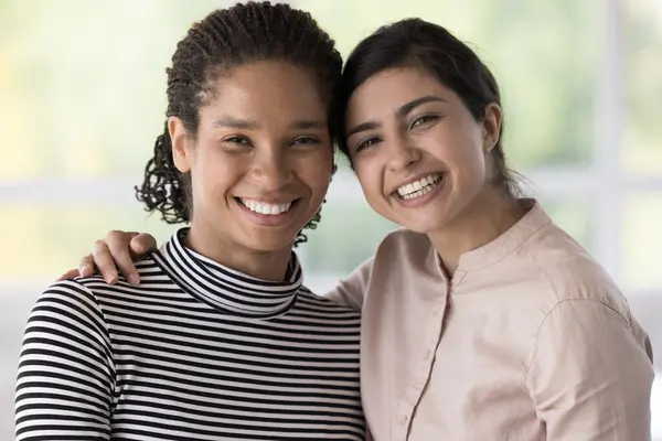 stock image Portrait of young cheerful attractive multiethnic women standing indoors, pose and hugging, looking at camera, feel happy, enjoying meeting, showing unity, interracial strong friendship, best friends