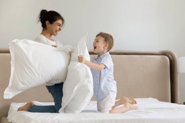 Yatak odasında yastık kavgası yapan mutlu Hintli anne ve Kafkasyalı aile evde eğlenceli aktiviteler yapıyor, gülüyorlar genç anne ve 7 'nin çocuğu eğleniyor, boş zamanlarının tadını çıkarıyorlar.