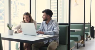 İki iş arkadaşı birlikte dizüstü bilgisayar kullanıyor, video içeriği izliyor, notlar yazıyor, ortak çalışma kafesinde bilgisayarın başında oturuyor, iş görevlerini, proje planını, takım çalışmasını, çevrimiçi iletişimi tartışıyor.