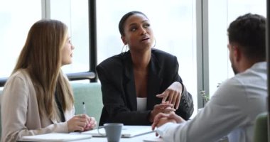 Kendine güvenen çekici Afrikalı yönetici kadın iş ortağıyla konuşuyor, iş adayıyla görüşüyor, konuşuyor, dinliyor, başını sallıyor, gülümsüyor. Şirkette kariyer tartışması yapan çok ırklı meslektaşlar