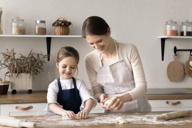 Anne ve küçük kızı evde birlikte yemek pişirmek için önlük giyiyorlar, ev yapımı çörekler için hamur yapıyorlar, konuşuyorlar ve yemek yapıyorlar. Sevgi dolu anne, anaokulu çocuğuna aşçılık becerileri öğretiyor. Annelik, aşçılık.