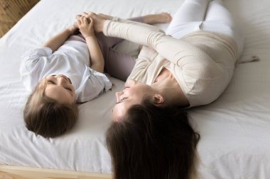 Genç mutlu anne ve küçük kızın yakın plan çekimleri yatak odasında zaman geçirir, rahat bir yatakta uzanır, iletişim kurar, sabahın erken saatlerinde evde birlikte eğleniriz. Aile bağları, bağ, kaygısız eğlence.