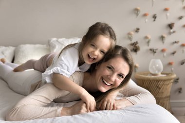 Anaokulu 4 'ün kızı gülüyor, annesine uzanıyor, kameraya bakıyor, birlikte tasasız bir sabah geçiriyorlar rahat, modern bir yatak odasında yatakta dinleniyorlar. Aile hafta sonu eğlencesi, tasasız, sağlıklı gündüz uykusu, birlik.