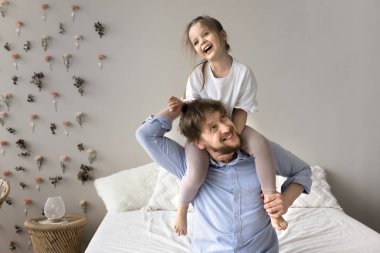 Genç babaların omuzlarında oturan sevimli 4 'lü kızlar gülüyor, eğleniyor, heyecanlanıyor ve çok eğleniyorlar modern, güzel yatak odasında keyifli vakit geçiriyorlar. Oyun zamanı, babalık, velayet