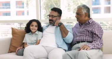 Pozitif Hintli büyük baba ve büyükbaba sevimli küçük kız torununu izliyor, çocukla konuşuyor, kanepede oturuyor, aile eğlencesi, çocuk bakımı, iletişim kuruyor.