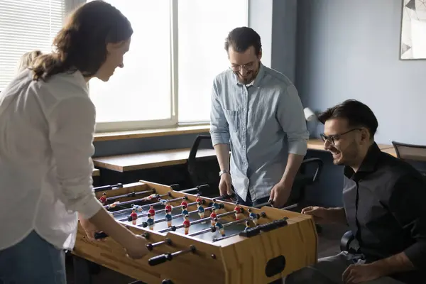 stock image Happy joyful teammates, friendly colleagues having fun at workplace. Group of cheerful employees playing table soccer during lunch break, gathered together laughing, enjoy tabletop football in office