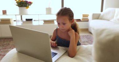 Odaklanmış Latin anaokulu öğrencisi kız dizüstü bilgisayarda öğrenme oyunu oynuyor, ebeveynsel kontrol modu üzerinde, evde tek başına bilgisayar kullanıyor, kanepede dinleniyor, çevrimiçi içerik izliyor, film, çizgi film, dokunmatik dokunmatik dokunmatik ped