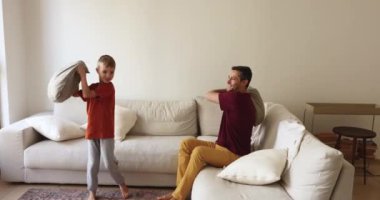 Mutlu, pozitif bir Latin baba ve aktif küçük oğlu oturma odasında kavga ediyor, yastık savaşında birbirlerini dövüyorlar, gülüyorlar, eğleniyorlar, eğleniyorlar, eğlenceli aile oyunları, çocukluk.