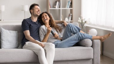 Neşeli İspanyol çift oturma odasında kanepede oturuyor, birlikte vakit geçiriyorlar, uzaktan kumandayı tutuyorlar, TV izliyorlar, gülüyorlar, komik komedi filmlerinden zevk alıyorlar, online yayın hizmetlerinden faydalanıyorlar. Eğlence, eğlence.