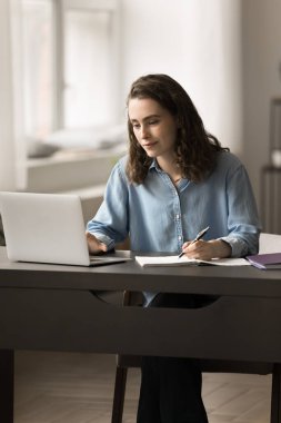 Odaklanmış liseli kız masada dizüstü bilgisayarla çalışıyor, üniversite sınavına ya da lise sınavına hazırlanıyor, deneme yazıyor, ev ödevi yapıyor, ödev öğreniyor, notlar alıyor. Eğitim, modern teknoloji