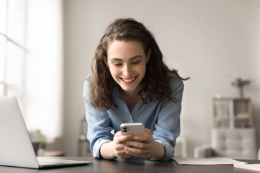 İş yerinde modern akıllı telefonu kullanan gülümseyen genç bir kadın, masaya yaslanmış, mesaj alışverişinden zevk alan, işten uzaklaşan ya da internete takılan, arkadaşlarıyla sohbet eden, haber akışı yapan. Teknoloji