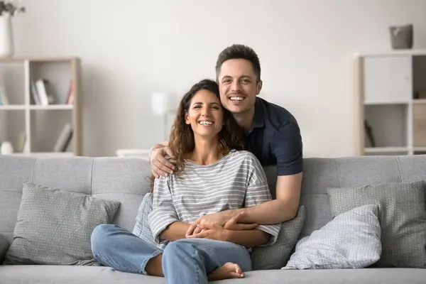 stock image Portrait of wellbeing family posing for camera. Handsome Hispanic husband hugs his lovely Latina wife sit on sofa spend time together, feel happy, satisfied with strong marriage and harmonic relations