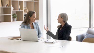 Üst düzey iş kadını dizüstü bilgisayardaki çalışana danışmanlık yapıyor, büyük çalışma masasında oturuyor, konuşuyor, işbirliği stratejisini anlatıyor. Genç ve yaşlı meslektaşlar ofiste konuşuyor.