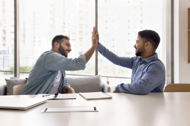 İki neşeli çok ırklı iş arkadaşı ofis masasında beşlik çakıyor takım çalışması başarısı, başarılı işbirliği, kurumsal arkadaşlığın tadını çıkarma, etkili ortaklık, takım çalışması sayesinde.