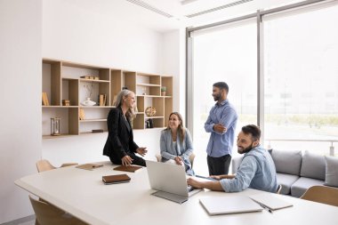 Beyaz renkli modern ofis içinde mutlu iş adamları buluşması, büyük masada oturmak, konuşmak, gülmek, eğlenmek, proje üzerinde beyin fırtınası yapmak, fikirler tartışmak.