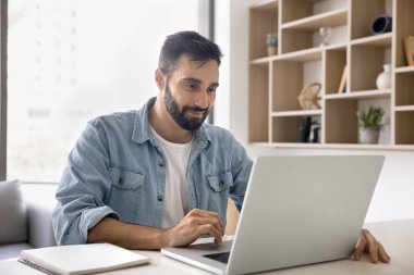 İş yerindeki dizüstü bilgisayarında çalışan genç, pozitif İspanyol iş adamı profesyonel uygulama, internet iletişimi için yazılım, çevrimiçi bağlantının keyfi, iş teknolojisi, gülümseme
