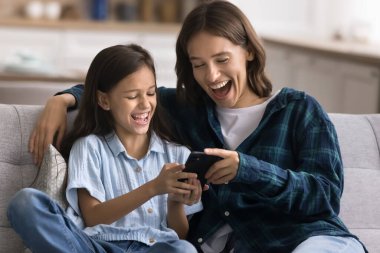 Neşeli genç bir anne ve mutlu şirin bir kız çocuğu akıllı telefonuyla internet üzerinden iletişim kuruyor, internette video izliyor, eğleniyor, sevinç çığlıkları atıyor.