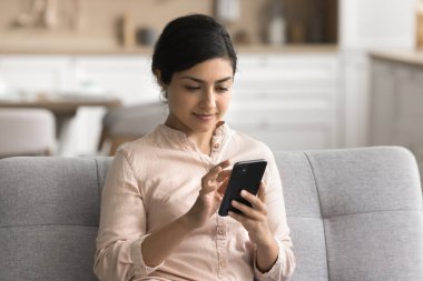 Modern akıllı telefonu elinde tutan genç Hintli kadın İnternet 'te vakit geçiriyor, evden alışveriş yapmanın rahatlığını yaşıyor, internette eşyalar alıyor, programları yönetiyor, mobil uygulama kullanarak plan yapıyor.
