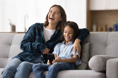 Mutlu, heyecanlı, genç bir anne, sevimli, akıllı kızına cep telefonu kullanarak sarılıyor. Anne ve çocuk evde dinleniyor, eğleniyor, iletişim için akıllı telefon uygulamasını kullanıyor.