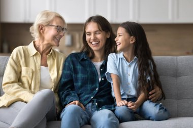 Mutlu çocuk, anne ve büyükanne evde buluşuyor, rahat koltukta konuşuyor ve gülüyor, sevgi, sıcaklık, ilgi, aile ilişkilerinden keyif alıyor,