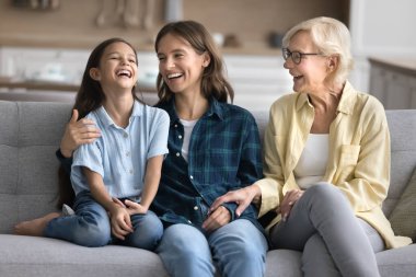 Mutlu güzel kız, şefkatli genç anne ve neşeli büyükanne evde konuşuyor ve gülüyor, rahat koltukta oturuyor, sohbet ediyor, eğleniyor, aile iletişiminden keyif alıyor,