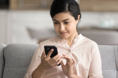 Hintli kadın kanepeye uzanmış akıllı telefon kullanıyor, e-posta okuyor, mesajları kurye ile paylaşıyor, eğlence için yeni mobil uygulamalar indiriyor, arama ya da sipariş yapıyor, hafta sonları internette vakit geçiriyor.