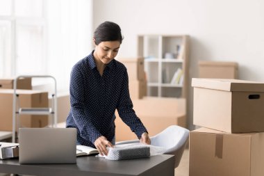 Ciddi genç Hintli kadın, küçük işletme sahibi satın aldığı malları paketliyor, güvenlik için baloncuklu ambalajla örtüyor, karton bir kutuda müşteriye gönderiyor, depoda çalışıyor. Ticaret, KME, sevkiyat