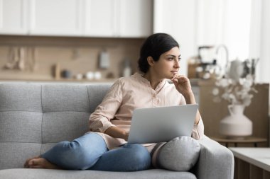 Düşünceli Hintli kadın yaratıcı fikirler üzerinde düşünüyor, bilgisayarla koltukta çalışıyor ya da çalışıyor, düşüncelerin derinliklerine bakıyor, arama sorunu çözümü, tele çalışma, post metin üzerinde kafa yoruyor. Serbest, teknoloji.