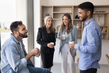 Neşeli çeşitli iş arkadaşları ofis yerinde kahve molasında konuşuyor ve gülüyor, rahatlığın, rahatlığın, ofis arkadaşlığının, resmi olmayan sohbetin, takım çalışmasının başarısını tartışıyorlar.