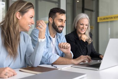 Üç iş arkadaşı dizüstü bilgisayarda buluşuyor, yazılım, web sitesi, başvuru sunumu ekranda, gülümsüyor, gülüyor, çalışma masasında oturuyor. Web tasarımcısı proje gösteriyor
