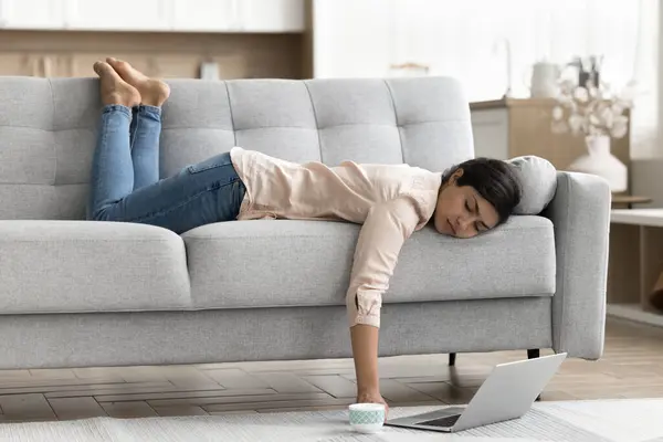 stock image Young Indian woman working or studying on laptop, feel exhausted, without energy or motivation looks overworked fell asleep lying on sofa. Boring weekend alone at home, procrastination, daytime nap