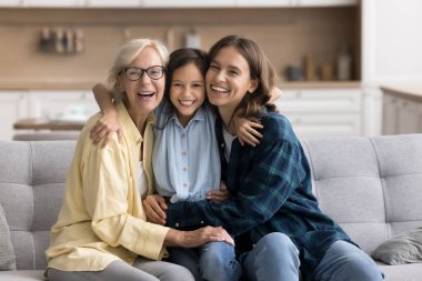 Neşeli kız, genç anneye sarılıyor ve evde kanepede oturmuş, dişlek bir gülümsemeyle kameraya bakıyor. Üç kuşak kadın aile portresi