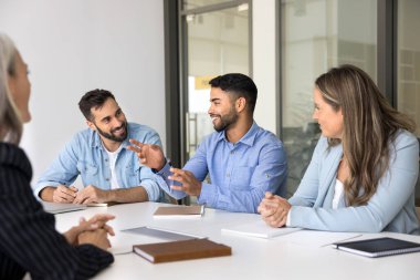 Neşeli genç Arap iş adamı çeşitli iş arkadaşlarıyla toplantıda konuşuyor, yaratıcı fikirler anlatıyor, işbirliği üzerine beyin fırtınası yapıyor, takım çalışmasını tartışıyor, gülümsüyor, gülüyor.