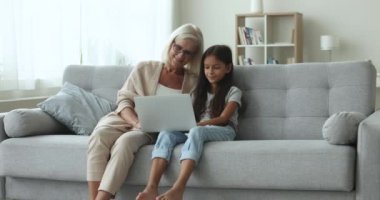 Mutlu torun çocuk ve neşeli sarışın büyükanne birlikte online medya servisini kullanıyorlar, daktilo ediyorlar, gülüyorlar, komedi filmi izliyorlar, internette komik aile dizileri izliyorlar.