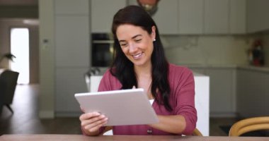 Güzel, genç bir kadın, dijital tabletle rahat bir mutfakta oturur, modern cihazlar kullanır, arkadaşlarıyla sohbet eder, haberleri paylaşır, uzaktan çalışan müşterilerle haberleşir, internette kaygısızca vakit geçirir.