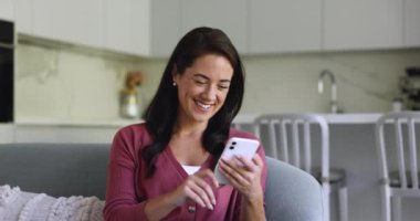 Gülümseyen genç Latin kadın evdeki kanepede oturur modern akıllı telefon kullanarak arkadaşınla internet üzerinden konuşmanın keyfini çıkarır, mesajları kurye aracılığıyla paylaşır, hoş haberler okur, mesajlara cevap verir, uzaktan sohbete öncülük eder.