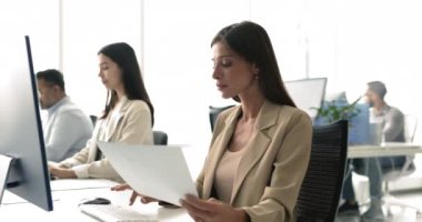 İşyerinde çalışan, kağıt tutan, evrak hazırlayan, sözleşme metnini hazırlayan, veri analizi yapan, müşteri için sunum yaratan, belgeleri gözden geçiren odaklanmış kadın ofis çalışanı.