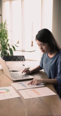 Genç iş kadını, kağıtlarda sunulan dosya ve diyagramlarla ilgili bilgi ve analizlerle ilgilenen masasında oturuyor, görsel bilgileri karşılaştırıyor, daha fazla araştırma yapıyor, analiz yapıyor, dizüstü bilgisayar kullanıyor.