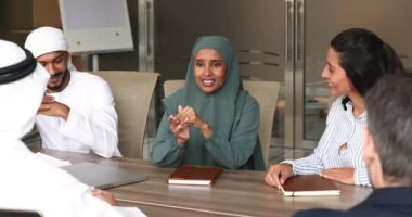 Mutlu Arap iş kadını tesettüre ve Müslüman kumaşına bürünmüş, büyük masada çeşitli iş arkadaşlarıyla konuşuyor, ortaklarla görüşüyor, proje üzerinde beyin fırtınası yapıyor, takım çalışmasını tartışıyor.