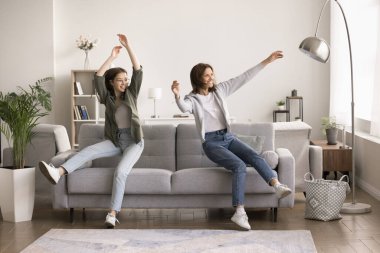 Neşeli genç kız ve anne, şık bir oturma odasında kanepeye çömelmiş, eğleniyor, evde kaygısız bir hafta sonu tatili geçiriyorlar, mutlu oluyorlar, tatil konaklamalarında neşeli bir ruh hali içindeler.