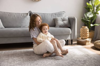 Mutlu genç anne, rahat bir oturma odasında yerde oturur, kucağına oğlunu alır, sevgisini, sıcaklığını ve bakımını ifade eder, iletişim kurar, aktif aile hafta sonunun ve zihinsel bağlantının tadını çıkarır. Annelik, şefkat, çocukluk.