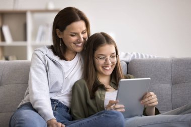 Genç kızı olan gülümseyen bir kadın rahat bir koltuğa oturur, dijital tablet kullanır, yeni uygulamanın tadını çıkarır, film izler, sosyal ağda komik videolar izler, internette gezinir. İki nesildir mutlu olan aile modern aletlerin tadını çıkarsın.