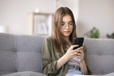 Ciddi bir genç kız cep telefonunu evde kullanıyor, televizyon ve televizyon platformlarında video izliyor, mobil oyunlar oynuyor, kurye aracılığıyla arkadaşlarıyla sohbet ediyor. Modern aletler aşırı kullanım, kötü alışkanlık