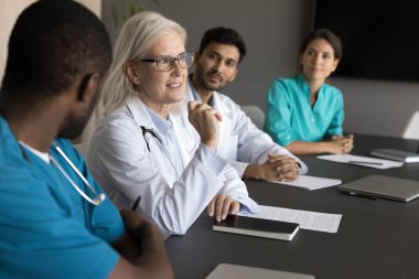 Seminerde veya tıp konseyi toplantısında tartışmalara katılan bir grup doktor, tecrübeli yaşlı kadın doktorların görüşlerini meslektaşlarıyla paylaşıyor. Bilgi alışverişi, profesyonel etkileşim.