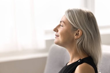 Huzurlu, olgun bir kadının temiz hava soluyup manzarayı kapattığı bir yan profil. Kadın gözlerini kapar rahatlamak, huzur bulmak ve iç huzurunu arttırmak için bir an bekler. Farkındalık