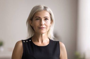Orta yaşlı iş kadını kameraya ciddi yüz ifadesiyle, ayakta durarak, ofiste poz vererek, yakın plan portresiyle bakar. Orta yaş, doğal güzellik, mesleki meşguliyet profil fotoğrafı