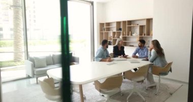 Dört müdürden oluşan çeşitli iş adamları toplantı masasında konuşuyor ve gülüyor, yaratıcı fikirler üzerinde beyin fırtınası yapıyorlar, takım çalışmasının keyfini çıkarıyorlar, modern ofis müzakere odasında işbirliği yapıyorlar.