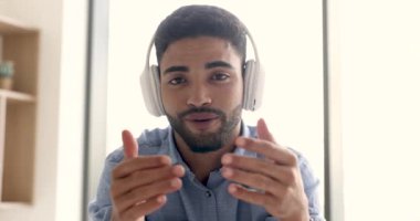 Büyük kablosuz kulaklıklı mutlu genç Arap blogcu video konferansında konuşuyor, iletişimin keyfini çıkarıyor, internet teknolojisini yayın ve yayın için kullanıyor.