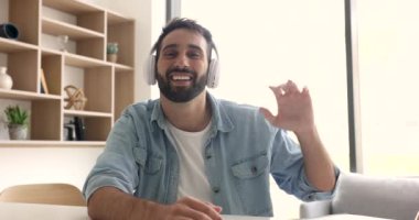 Neşeli genç Latin serbest çalışan kulaklıklı adam evden video konuşmaları yapıyor internet iletişimini online sohbet için kullanıyor selamlaşma elini sallıyor merhaba, gülümsüyor, kameraya bakıyor.