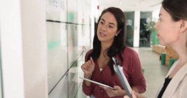 İki iş kadını, notlar ve bilgilerle dolu bir tahtanın önünde sohbet ediyorlar. Birlikte çalışan meslektaşlar, anahtar noktaları belirlemek, strateji oluşturmak, ofiste işbirliği planlamak